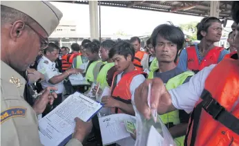  ??  ?? PAPERS, PLEASE: Local officials conduct identity checks before a fishing crew heads out to sea.