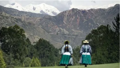  ?? — AFP ?? LA PAZ: This file photo shows two Aymara indigenous women walk through the green of La Paz Golf Club, as the Illimani’s snow summit appears on the background.