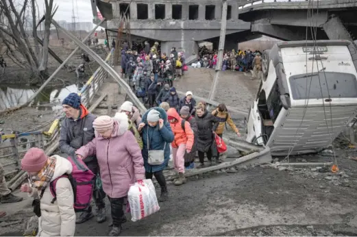  ?? VADIM GHIRDA/AP ?? People cross on an improvised path under a bridge that was destroyed by a Russian airstrike while fleeing the town of Irpin, Ukraine, on Saturday.