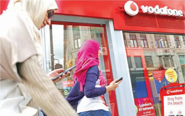  ?? Reuters ?? ↑
People pass a Vodafone store in London.