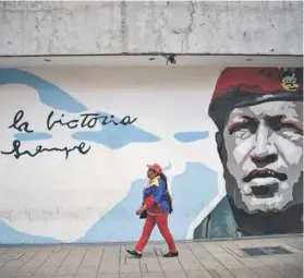 ??  ?? ► Un partidario del PSUV camina junto a un grafiti de Chávez.