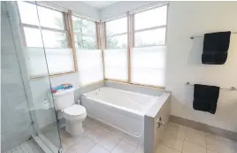  ??  ?? • The roomy grey-and-white bathroom has large corner windows, but remains private thanks to Hunter Douglas blinds that operate in both directions. Porcelain tiles are on the floor and around the tub.