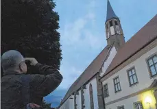  ?? FOTO: BERNHARD HAMPP ?? Ein Mann beobachtet in der Dämmerung Fledermäus­e im Klosterhof von Kirchheim am Ries.