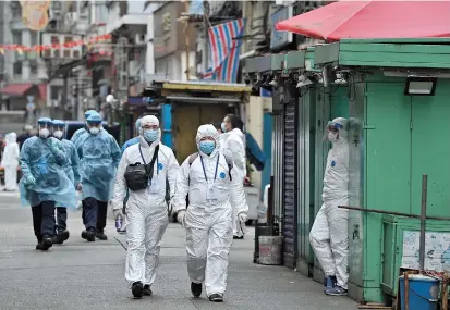  ??  ?? Health workers in white hazmat suits walk along a street as authoritie­s tested residents for a second day in the Jordan area of Hong Kong on Sunday. The city’s first COVID-19 lockdown as lifted yesterday after testing thousands of residents living in the area. — AFP