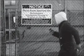  ?? The Associated Press ?? FLOOD ZONES: A man jogs past a notice for the Martin Aaron Inc. Superfund site on Dec. 11 in Camden, N.J. Nearly 2 million people in the U.S. who live within a mile of 327 Superfund sites in areas prone to flooding or vulnerable to rising seas caused...