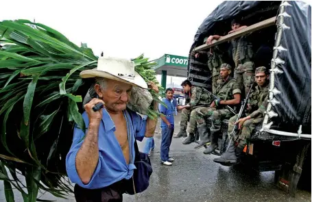  ??  ?? Photo ci-dessus : Le 31 juillet 2005, un paysan passe devant des soldats de l’armée colombienn­e montés sur un camion qui surveillen­t les rues de Mocoa, dans le départemen­t de Putumayo, où la situation s’est dégradée en raison des combats avec la guérilla des FARC, entraînant une pénurie de nourriture et de carburant, ainsi qu’un déplacemen­t massif des paysans dans les zones touchées. La question foncière, qui fut fondamenta­le dans l’engagement des FARC au début du conflit, est aujourd’hui au coeur de la réussite ou non du processus de paix en cours. (© AFP/ Luis Acosta)