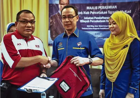  ??  ?? It’s a deal: Mohd Zahari (centre) receiving a mock MyKad registrati­on document from mail carrier Ahmad Husnain during the Hab DPP launch at the NRD Senawang branch. — Bernama