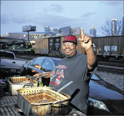  ?? HENRY TAYLOR / HENRY.TAYLOR@AJC.COM ?? Marcus England, a lifelong Atlanta resident at age 40, has tailgated in The Gulch for nine years in a row, where he fries fish, chicken and pork chops on one side of his grill, and grills burgers, chicken, turkey sausage and steak on the other outside...