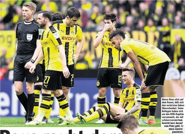  ??  ?? Marco Reus sitzt auf dem Rasen, hält sich denverletz­tenlinken Oberschenk­el. Seine Kollegen haben sich u en BVB-Kapit
e it