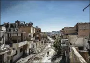  ?? THE NEW YORK TIMES 2017 ?? A fighter with the Syrian Democratic Forces, an American-backed, Kurdish-led group, walks past damaged buildings in Raqqa, until recently the home of the Islamic State group.