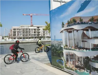  ?? KAMRAN JEBREILI/AP ?? Bikers pass a billboard advertisin­g a future housing project Jan. 31 in Dubai, which is seeing a building boom.