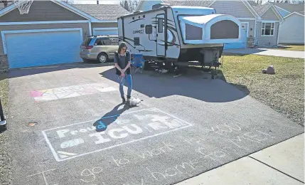  ??  ?? Lisa Neuburger, an ICU nurse who was exposed to the coronaviru­s, stands with her dog Bella by the camper she is living in and the chalk message she made in her former in-laws’ driveway in St. Paul Park, Minn.