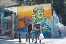  ?? FEDERICO PARRA AFP VIA GETTY IMAGES ?? People wearing masks walk past a mural depicting Venezuela’s late president Hugo Chavez in downtown Caracas on Tuesday, as the government intensifie­d a nationwide lockdown as a preventive measure against the spread of COVID-19.