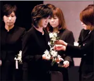  ??  ?? Eriko Okuda (center), whose son was killed by a tsunami one year ago, receives a chrysanthe­mum as relatives of tsunami victims offer flowers in front of the altar during the national memorial service in Tokyo on Sunday for the victims of the March 11,...