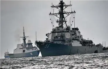  ?? Roslan Rahman / AFP / Getty Images ?? The USS John S. McCain, an American guided-missile destroyer, right, was left with a hole in its left side after a deadly collision with an oil tanker in waters off Singapore on Aug. 21. Nine sailors remain missing.