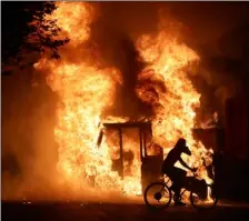  ?? SISTI/MILWAUKEE JOURNAL-SENTINEL VIA AP
MIKE DE ?? A man on a bike rides past a city truck on fire outside the Kenosha County Courthouse in Kenosha, Wis., on Sunday. Kenosha police shot a man Sunday evening, setting off unrest in the city after a video appeared to show the officer firing several shots at close range into the man’s back.