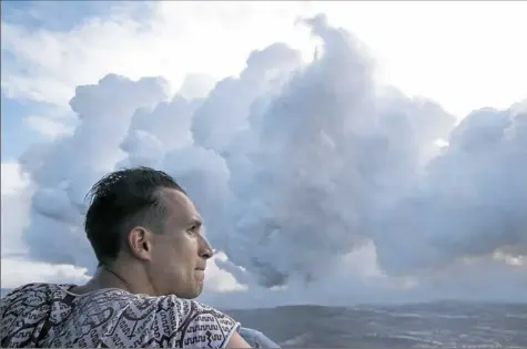  ?? Jae C. Hong/Associated Press ?? Gabor Kovacs, visiting from Hungary, watches as lava flows into the ocean, generating plumes of steam, near Pahoa, Hawaii, on Sunday. Kilauea volcano is oozing, spewing and exploding on Hawaii’s Big Island and has gotten more hazardous in recent days...