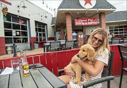  ?? Steph Chambers/Post-Gazette ?? Ashley Weiss, of the Strip District, holds her golden retriever, Colby, while enjoying a beverage with her boyfriend, Mark McMahon, of Baldwin, not pictured, on Friday at Double Wide Grill on the South Side. Despite indoor dining resuming in Allegheny County, many people decided to enjoy the nice weather and eat outside.