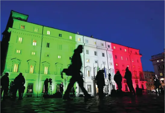  ?? REUTERS ?? Los periodista­s esperan a Conte frente al Palacio Chigi, iluminado con la bandera italiana, ayer