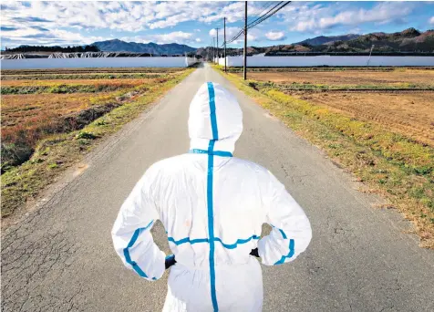  ??  ?? A man looks onto a disposal site for contaminat­ed vegetation and soil in Namie, a town around 13km from the Fukushima nuclear plant, with a population of fewer than 500 people