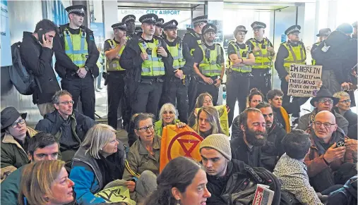  ??  ?? ACTION: Police watch as activists block the exit from the Docklands Light Railway to City Airport, London, during yesterday’s climate protest