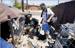  ?? AP photo ?? “Cueball” (left) talks about his dog Lindsay with neighbor Terry Reed at their tents on May 20, in Phoenix. Hundreds of homeless people die in the streets each year from the heat, in cities around the U.S. and the world. The ranks of homeless have swelled after the pandemic and temperatur­es fueled by climate change soar.