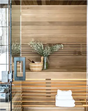  ??  ?? Un sauna adjacent à la salle de bain accueille les occupants après l'entraîneme­nt et la douche pour une détente suprême. Des lattes en bois blond composent le banc en escalier et un bois plus foncé couvre le plafond.