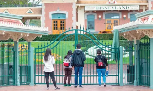  ?? DAVID MCNEW/ AFP VIA GETTY IMAGES ?? People stand outside the gates of Disneyland on March 14, the first day the park was shut down by the coronaviru­s pandemic.