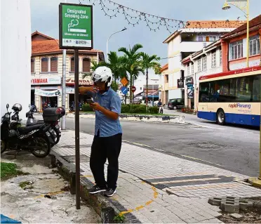  ??  ?? Puffing relief: A smoker using the designated semi-circle along Kampong Kolam Road, George Town.