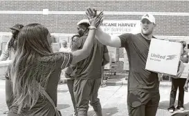  ?? Brett Coomer / Houston Chronicle ?? Anna Ucheomumu, left, high-fives Texans defensive end J.J. Watt after loading a car with relief supplies Sunday for people impacted by Hurricane Harvey. Several Texans helped Watt implement his relief efforts across the affected area.