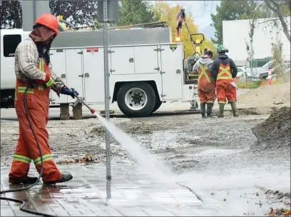  ?? JOE FRIES/Penticton Herald ?? City worker Joe Bravo washes mud off a sidewalk on Martin Street on Thursday afternoon following repair of a nearby water-main break.