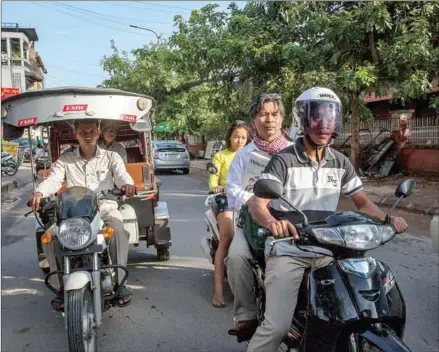  ?? OMAR HAVANA/THE NEW YORK TIMES ?? Minh Bui Jones rides on the back of a hired scooter while he delivers his magazine, October 25. in Phnom Penh, Cambodia, on