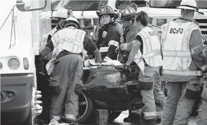  ?? JERRY JACKSON/BALTIMORE SUN ?? Baltimore County firefighte­rs look at a car pinned under a tractor-trailer on I-695 in Rosedale. Two seriously injured people were extricated after the accident.