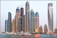  ?? BLOOMBERG VIA GETTY IMAGES ?? Top: The wave-shaped Jumeirah Beach Hotel in Dubai. Above: The Princess Tower (center) stands illuminate­d among other skyscraper­s in Dubai.