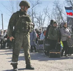  ?? ALEXANDER ERMOCHENKO / REUTERS FILES ?? A service member of pro-Russian troops stands guard in the southern port of Mariupol recently as evacuees wait before boarding
a bus to leave the city during Ukraine-Russia conflict.