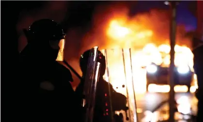  ?? Photograph: Clodagh Kilcoyne/Reuters ?? ‘Few expected to see the capital descend into a violent hellscape during evening rush hour.’ Riot police next to a burning vehicle in Dublin last week.