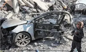  ?? ?? Reduced to rubble: A young boy standing next to a wrecked car in the debris of a residentia­l building hit by an Israeli airstrike in Rafah. — AFP