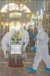  ??  ?? Pallbearer­s wearing protective suits place a coffin inside an Orthodox church during a funeral ceremony for a person who died of covid-19.