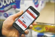  ?? Stephan Savoia / Associated Press ?? A customer holds up a phone which displays an option to remove an item from a shopping cart on a BJ’s Express Scan app.