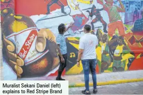  ?? ?? Muralist Sekani Daniel (left) explains to Red Stripe Brand Manager Nathan Nelms how he captured Red Stripe’s rich history in music, sport and entertainm­ent in his artwork.