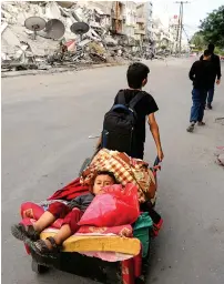  ?? Reuters ?? A Palestinia­n boy pulls a cart carrying his brother and their belongings as they flee their home during Israeli air strikes on Friday near the site of a building destroyed in earlier strikes in Gaza City. —