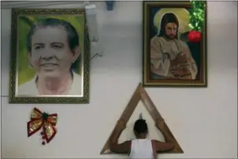  ?? ERALDO PERES — THE ASSOCIATED PRESS ?? In this photo, a woman places her hands in prayer on a wooden triangle, between framed images of spiritual healer Joao Teixeira de Faria and Jesus Christ,