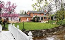  ?? ?? Flowering trees and evergreen trellises accent the soft rolling hills of the backyard, where stone paths lead to a paver-brick patio, a wooden gazebo and a wooden park bench. A keystone-lined stream with rock waterfalls winds through the property, and a white vinyl bridge arches over the stream to the wooded property.