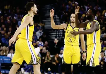  ?? (ES/GETTY IMAGES) ?? STEPHEN Curry #30 and Draymond Green #23 congratula­te fellow Warrior Klay Thompson #11 during a time out of their game against the New York Knicks at ORACLE Arena on January 08, 2019 in Oakland, California.