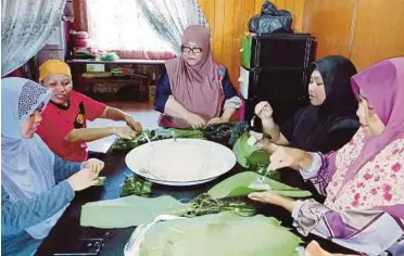  ??  ?? FATMAH (kanan) bersama ahli keluarga membungkus kelupis dengan menggunaka­n daun ngirik.