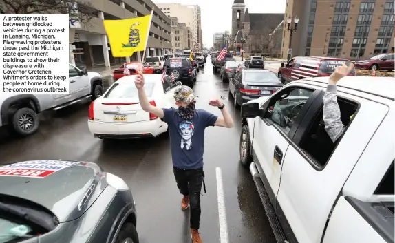  ??  ?? A protester walks between gridlocked vehicles during a protest in Lansing, Michigan. Flag-waving protesters drove past the Michigan state government buildings to show their displeasur­e with Governor Gretchen Whitmer’s orders to keep people at home during the coronaviru­s outbreak