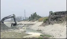  ?? HT PHOTO ?? A machine scooping out sand with the ‘dhussi bundh’ (right) just next to it on the river Sutlej in Moga on Monday.