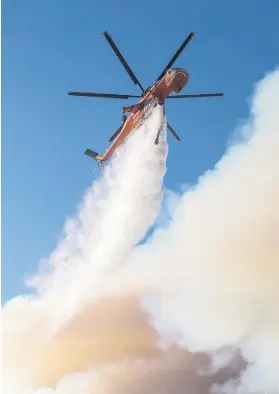  ?? Picture: EPA-EFE ?? KILLING POWER. A helicopter drops water over the fire in Bel-Air, California. An outbreak of several fires north of Los Angeles occurred as one of the strongest Santa Ana winds forecast for the season is ongoing and expected to last several days.