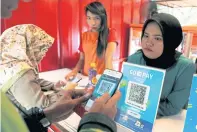  ??  ?? LEFT
A customer uses a smartphone to scan a QR code using Gopay at a food counter in Jakarta.