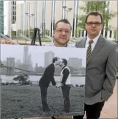  ??  ?? Tom Privitere (left) and his partner Brian Edwards pose at the federal courthouse in Denver on Wednesday with the engagement photo that was altered and used in a political campaign.